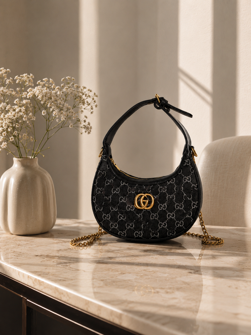 Noir crescent mini shoulder bag with gold chain on marble console